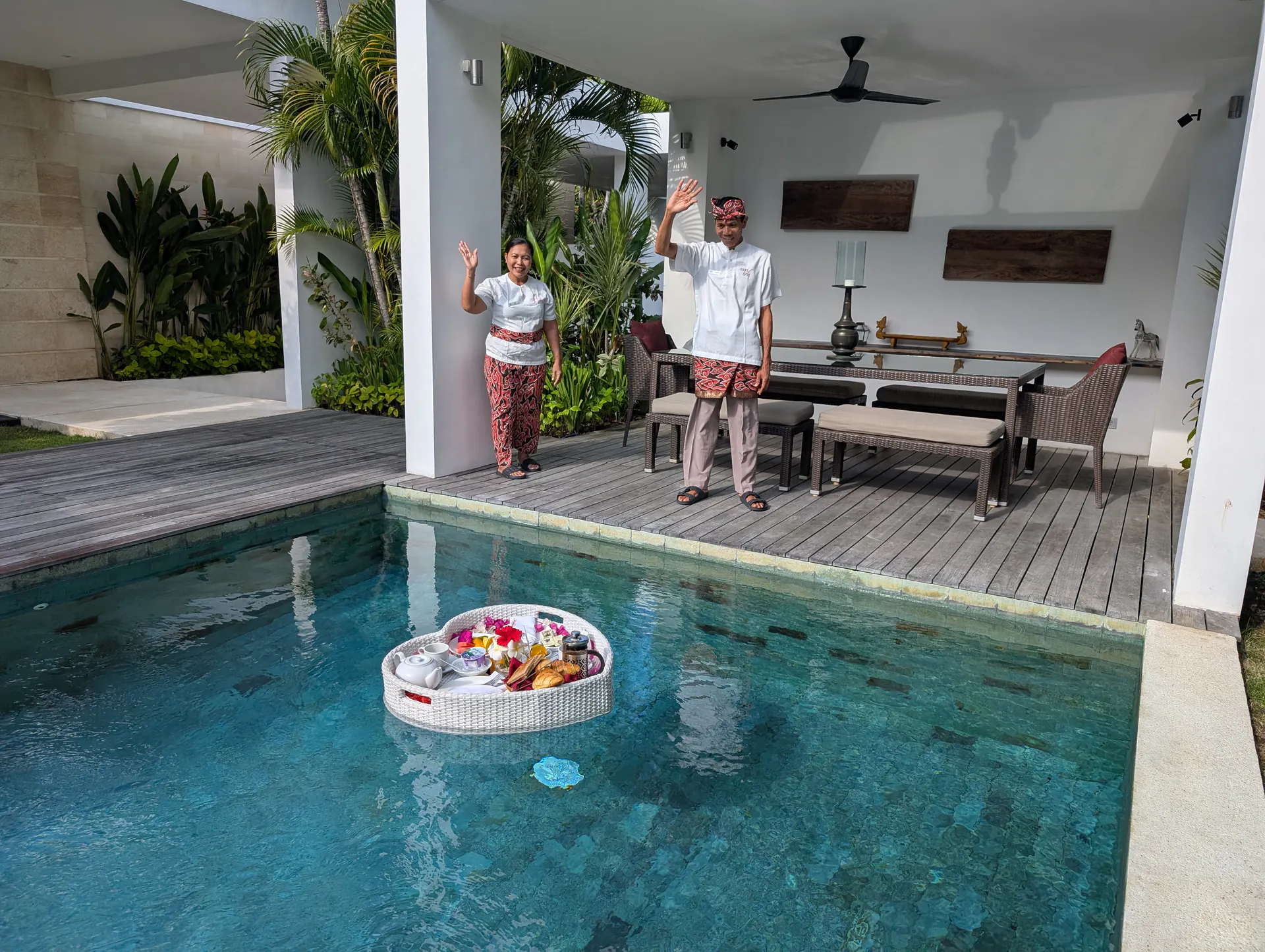A heart-shaped breakfast tray floating on the pool at Casa Brio, two of the villa team waving from the balé beyond