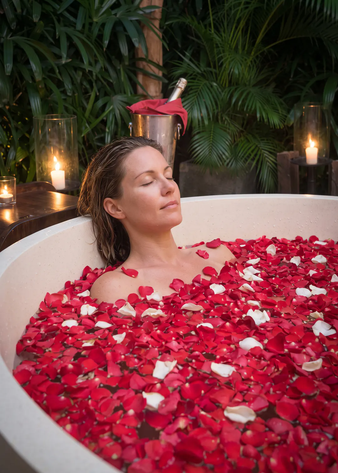 A guest in the circular terrazzo bath in the master courtyard at Casa Brio, filled with red and white petals and lit by candles