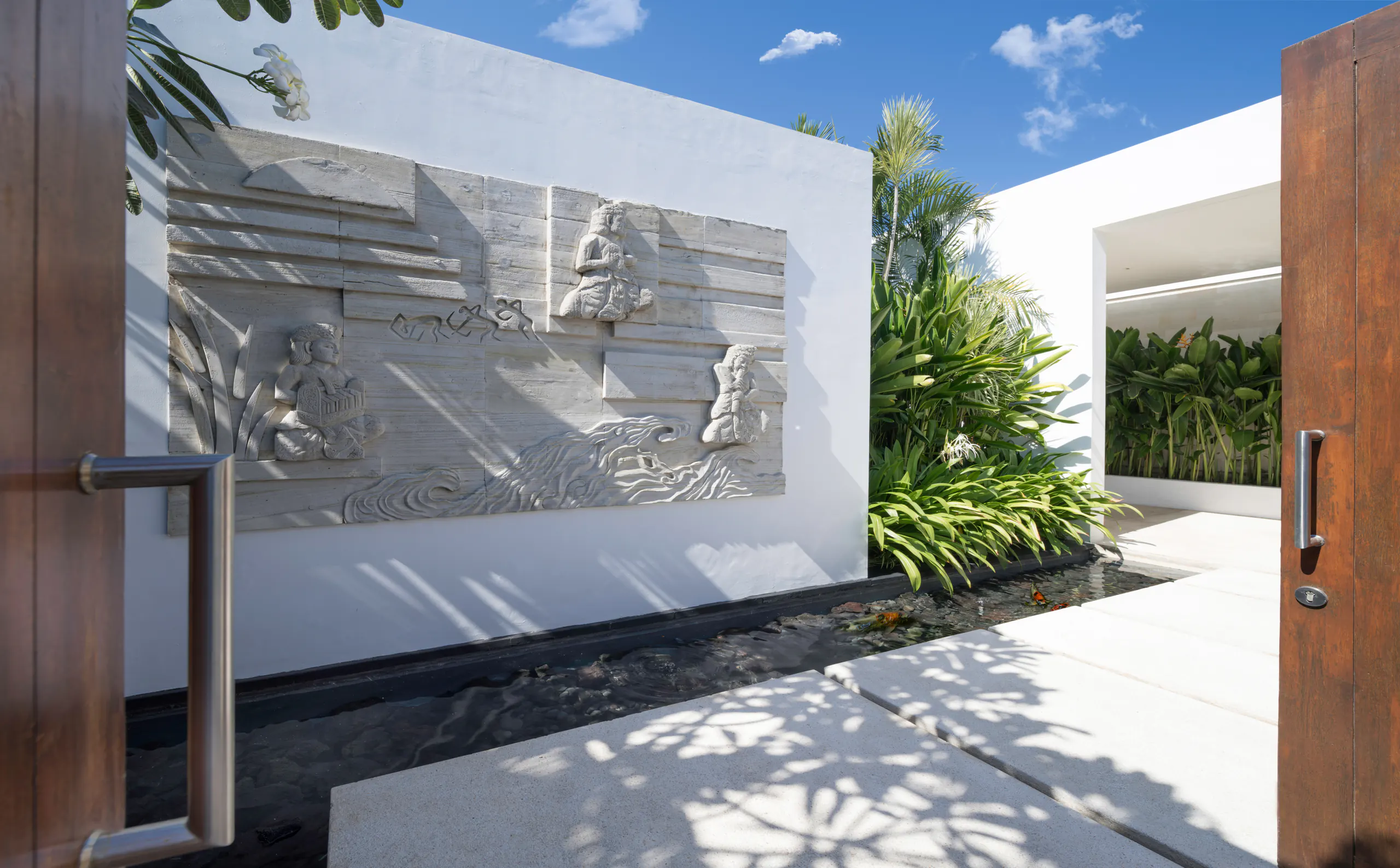The entrance walk at Casa Brio, a carved stone relief along the wall and the timber door standing open