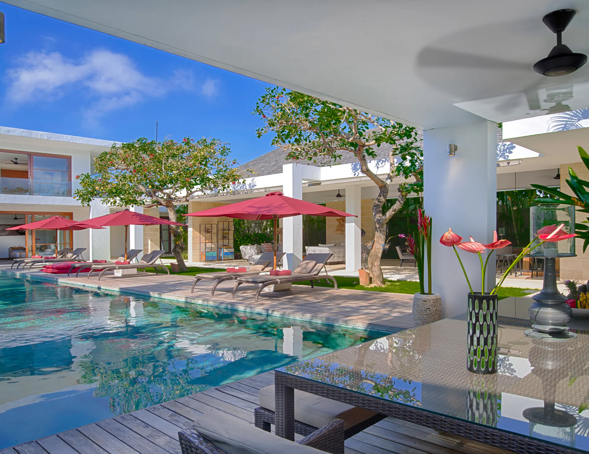 Looking down the pool at Casa Brio from the poolside dining table, anthurium in a vase and parasols along the deck
