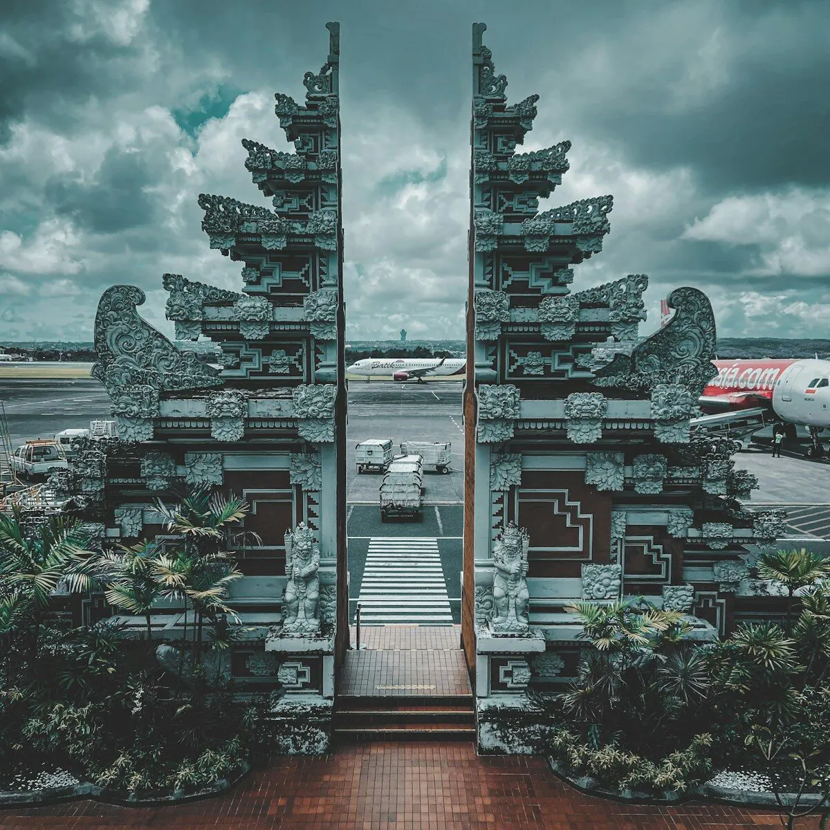 The carved split gate at Bali’s Ngurah Rai airport, a stone guardian each side and two airliners on the apron through the gap
