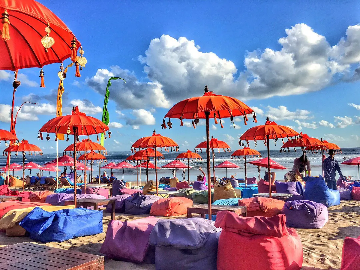 Rows of orange Balinese ceremonial parasols over pink and blue beanbags on the sand at Double Six Beach, the surf beyond