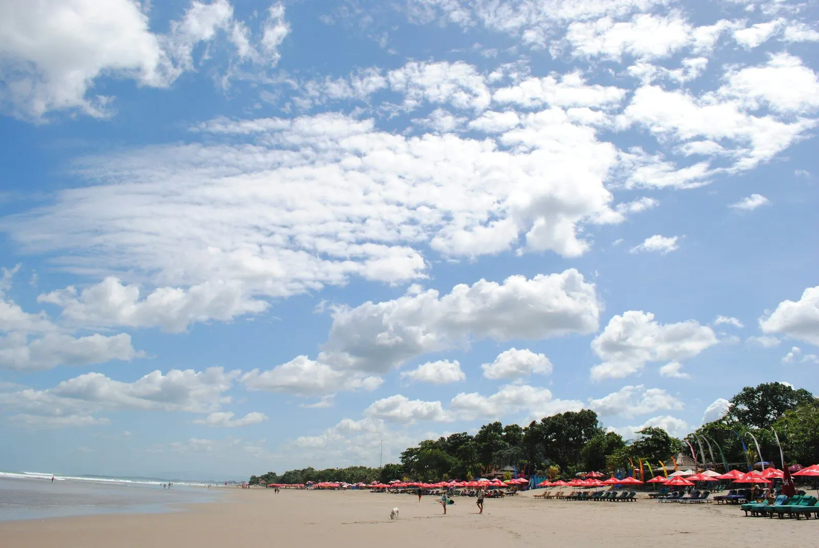 A wide stretch of grey-gold sand on Bali’s west coast, a long row of red parasols and timber loungers along the treeline