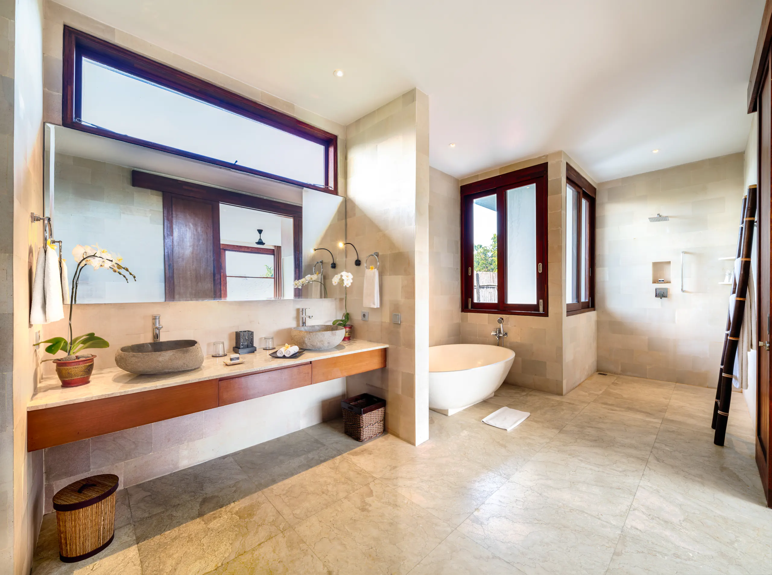A guest bathroom at Casa Brio, twin carved stone basins on a timber vanity, a freestanding tub under the window and a rain shower beyond
