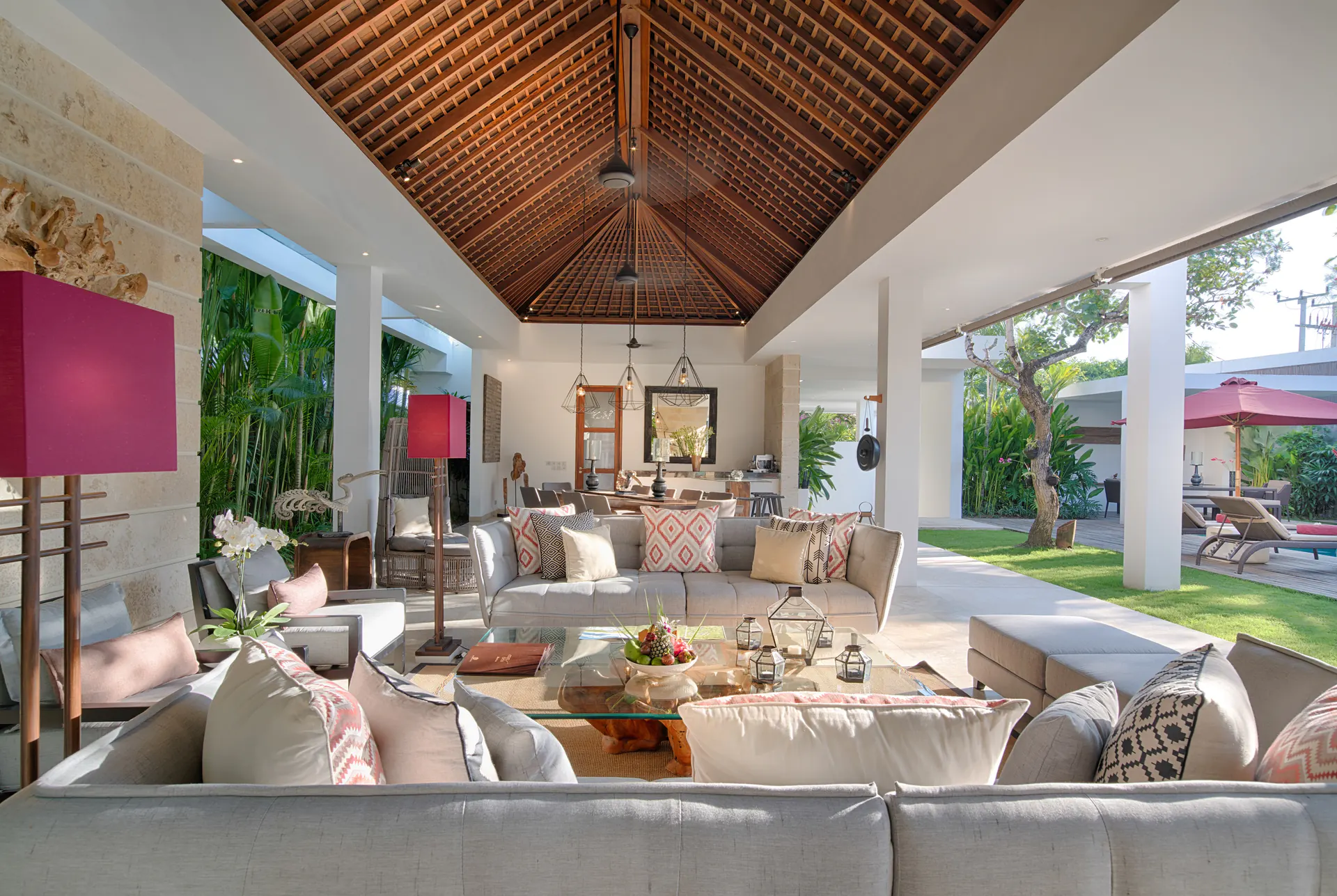 The living pavilion at Casa Brio down its length, sofas and coral ikat cushions under the pitched timber ceiling, the pool deck beyond